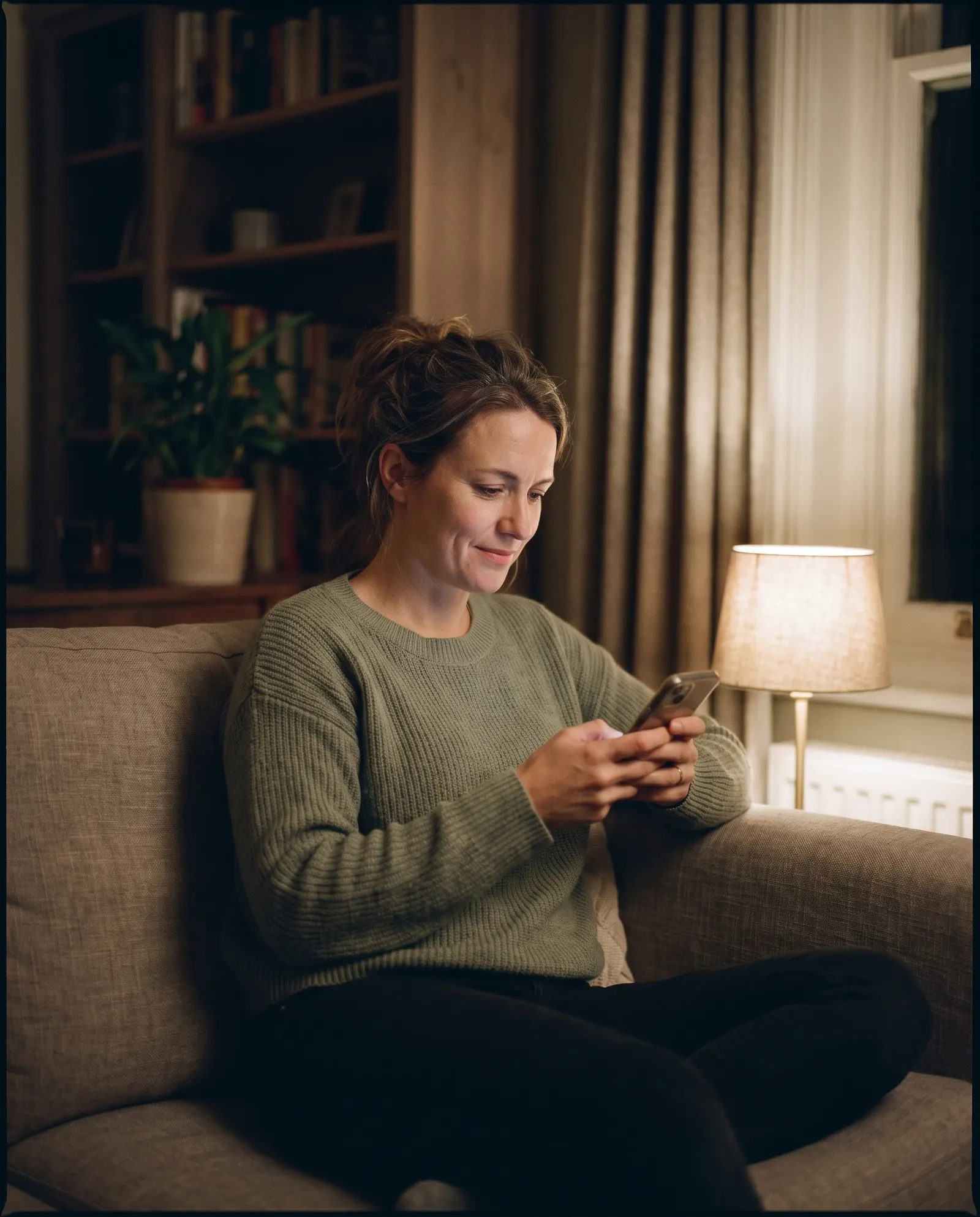 A woman reading her phone on a sofa in the evening.